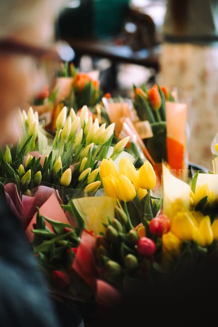 A vibrant display of fresh flowers at Belsize Park Flowers, featuring a variety of tulips in shades of yellow, cream, and pink, with some having closed buds and others fully open petals. The bouquets 